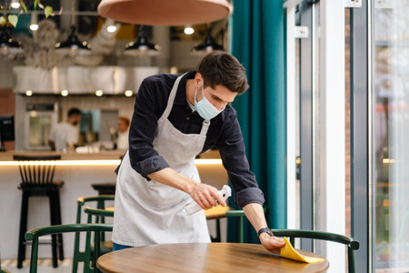 Man waiter wearing mask disinfecting table in the cafe indoorsの写真素材