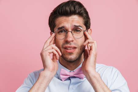 Young white man in eyeglasses with headache rubbing his temples isolated over pink backgroundの写真素材