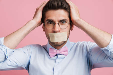 Young white man wearing bow tie posing with moth glued shut isolated over pink backgroundの写真素材