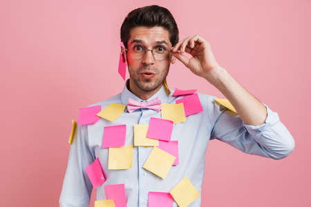 Young white man with stickers expressing surprise at camera isolated over pink background