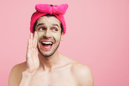 Young shirtless man wearing headband smiling and screaming at camera isolated over pink backgroundの写真素材