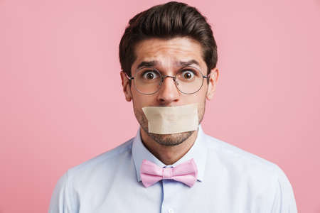 Young white man wearing bow tie posing with moth glued shut isolated over pink background