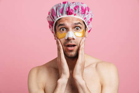 Young shirtless man with eye and nose patches expressing surprise at camera isolated over pink backgroundの写真素材