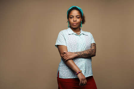 Young black woman in headband posing and looking at camera isolated over grey background