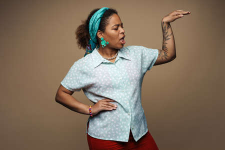 Young black woman in headband screaming and gesturing isolated over grey background