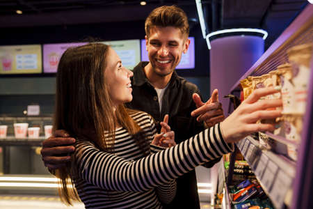 White young couple smiling while choosing snack together in cinema