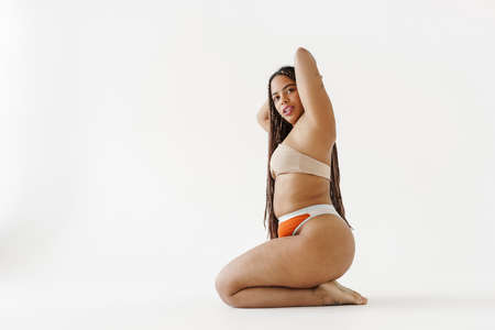 Smiling young african bodypositive woman in swimwear sitting over white backgroundの写真素材