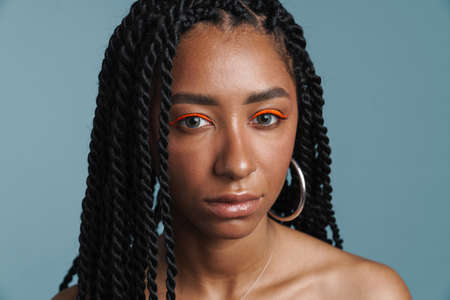 Shirtless black woman with makeup posing and looking at camera isolated over blue backgroundの写真素材