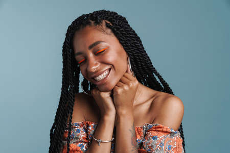 Young black woman with makeup smiling and posing at camera isolated over blue background