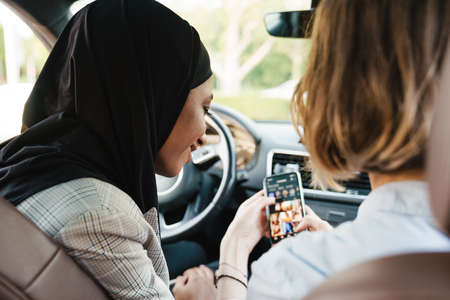 Two multiracial women using mobile phone while sitting in carの写真素材