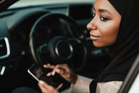 Black muslim woman wearing headscarf using cellphone while sitting in car
