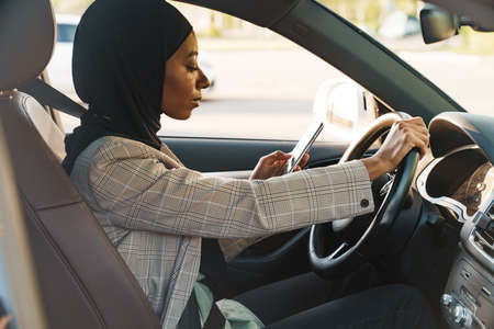 Black muslim woman wearing headscarf using cellphone while driving carの写真素材