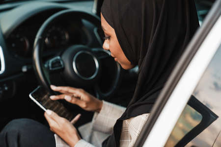 Black muslim woman wearing headscarf using cellphone while sitting in carの写真素材