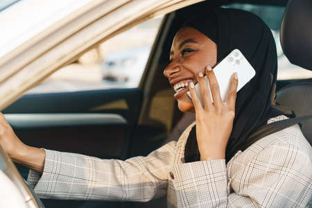 Black muslim woman wearing headscarf talking on cellphone while driving carの写真素材