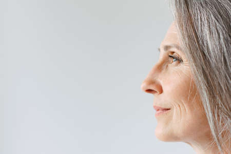Grey senior woman in t-shirt looking aside while posing in profile isolated over white background