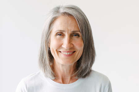 Grey senior woman in t-shirt smiling and looking at camera isolated over white background