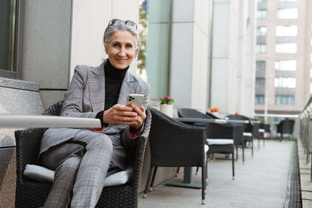 Grey white senior woman using mobile phone while sitting in cafe outdoorsの写真素材