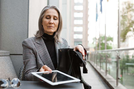 Grey white senior woman using tablet computer while sitting in cafe outdoorsの写真素材