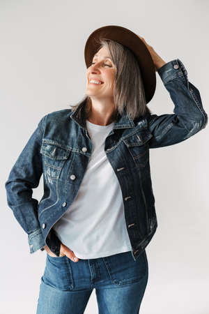 Grey senior woman smiling at camera while posing in hat isolated over white backgroundの写真素材