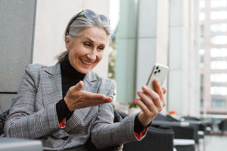 Grey white senior woman using mobile phone while sitting in cafe outdoorsの写真素材