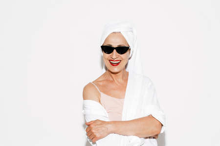 Senior woman in sunglasses smiling and looking at camera isolated over white wallの写真素材