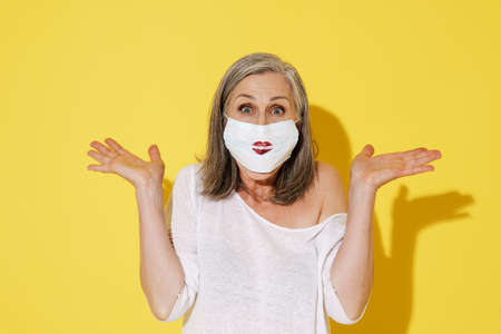 White senior woman posing in face mask showing copyspace at camera isolated over yellow wallの写真素材
