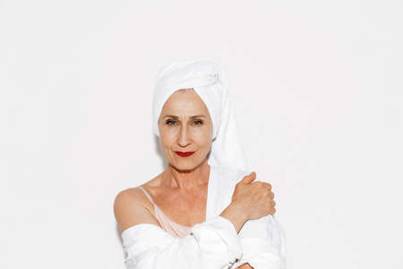 Senior woman wearing towel smiling and looking at camera isolated over white wallの写真素材