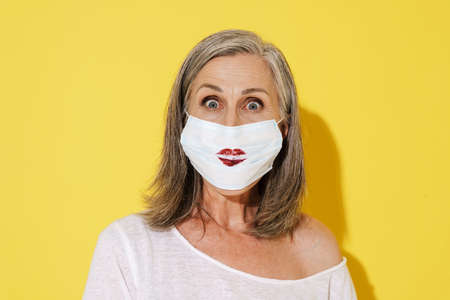 White senior woman posing in face mask expressing surprise on camera isolated over yellow wallの写真素材