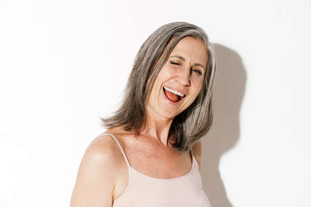 Mature grey woman laughing and winking at camera isolated over white wallの写真素材