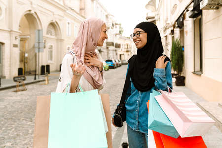 Two smiling mid aged islamic women in headscarves walking outside carrying shopping bagsの写真素材