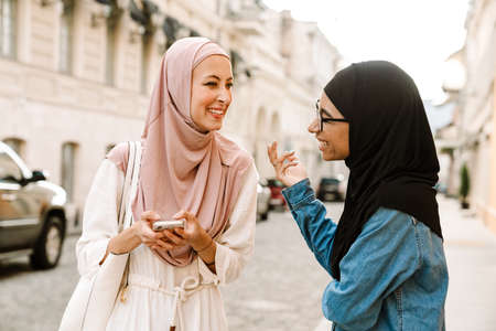 Multiracial muslim women wearing hijab talking while using mobile phone at city streetの写真素材