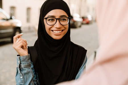 Two smiling young muslim women standing talking on a street close upの写真素材