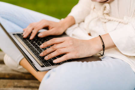 Close up of a young muslim woman in hijab sitting on a bench typing on laptop computerの写真素材