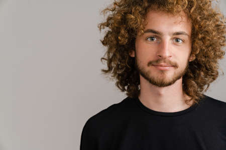 Young curly man with ginger hair posing and looking at camera isolated over grey backgroundの写真素材