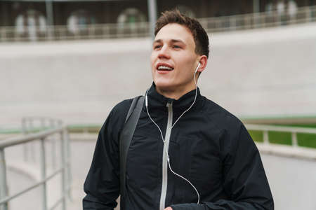 Happy young sportive man walking on stadium, carrying sport bag