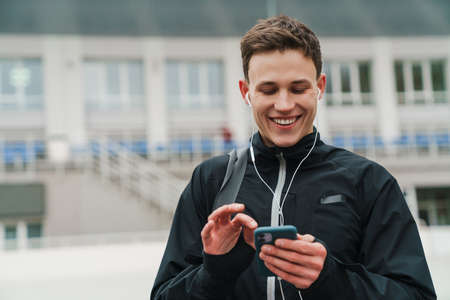 Handsome happy sportsman listening music with earphones and cellphone at stadium outdoors