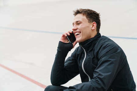 Attractive young sportsman using mobile phone while sitting at the stadium, resting