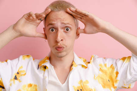 Young blonde man gesturing while expressing surprise at camera isolated over pink background