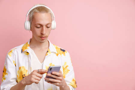 Young blonde man wearing headphones using mobile phone isolated over pink backgroundの写真素材