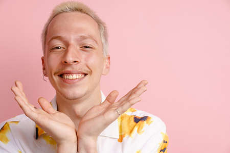 Young blonde man in shirt gesturing and smiling at camera isolated over pink backgroundの写真素材