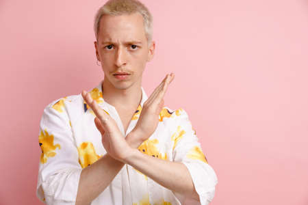 Young blonde man making stop gesture and looking at camera isolated over pink background