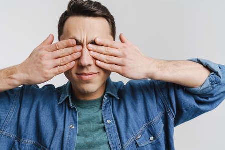 Young brunette man dressed denim shirt covering his ears isolated over white backgroundの写真素材