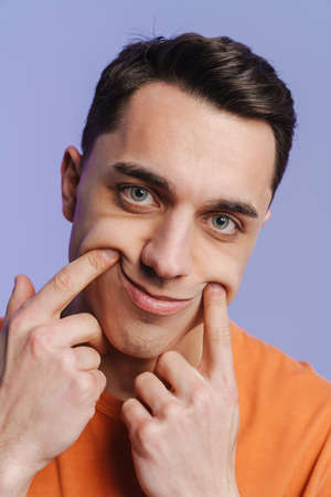 Young brunette white man making his smile with fingers isolated over purple backgroundの写真素材
