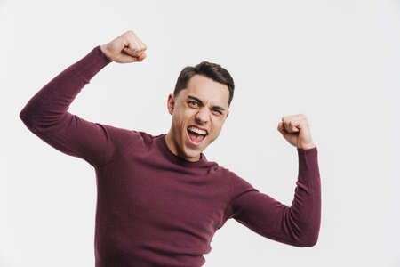 Young excited man screaming while making winner gesture isolated over white background