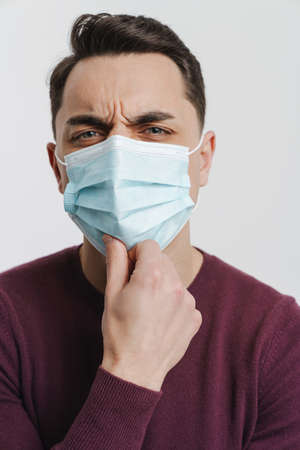 Young brunette man in face mask frowning and looking at camera isolated over white backgroundの写真素材