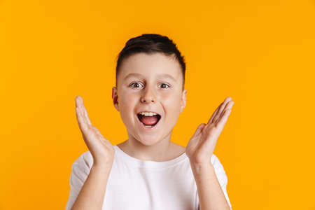 Happy smiling excited preteen boy in t-shirt standing over yellow background holding arms at face