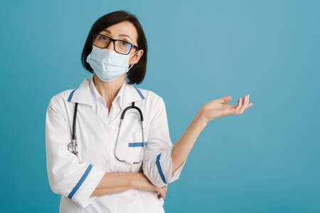 European mature doctor in face mask holding copyspace isolated over blue wallの写真素材
