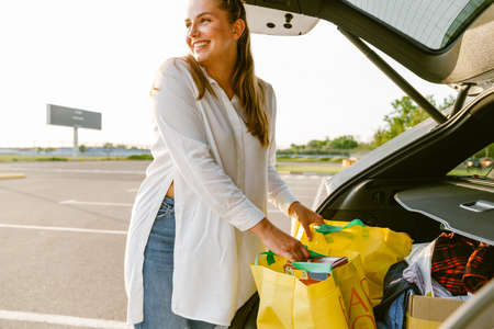 White woman smiling while getting shopping bag out of trunk at parking