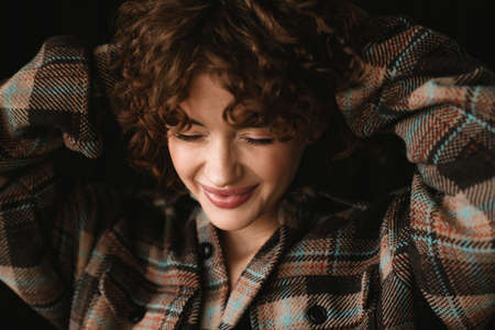 Smiling young redhead woman in plaid shirt standing in studio posing