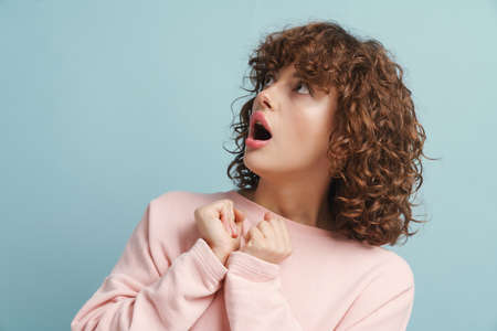 Young ginger shocked woman expressing surprise and looking aside isolated over blue backgroundの写真素材